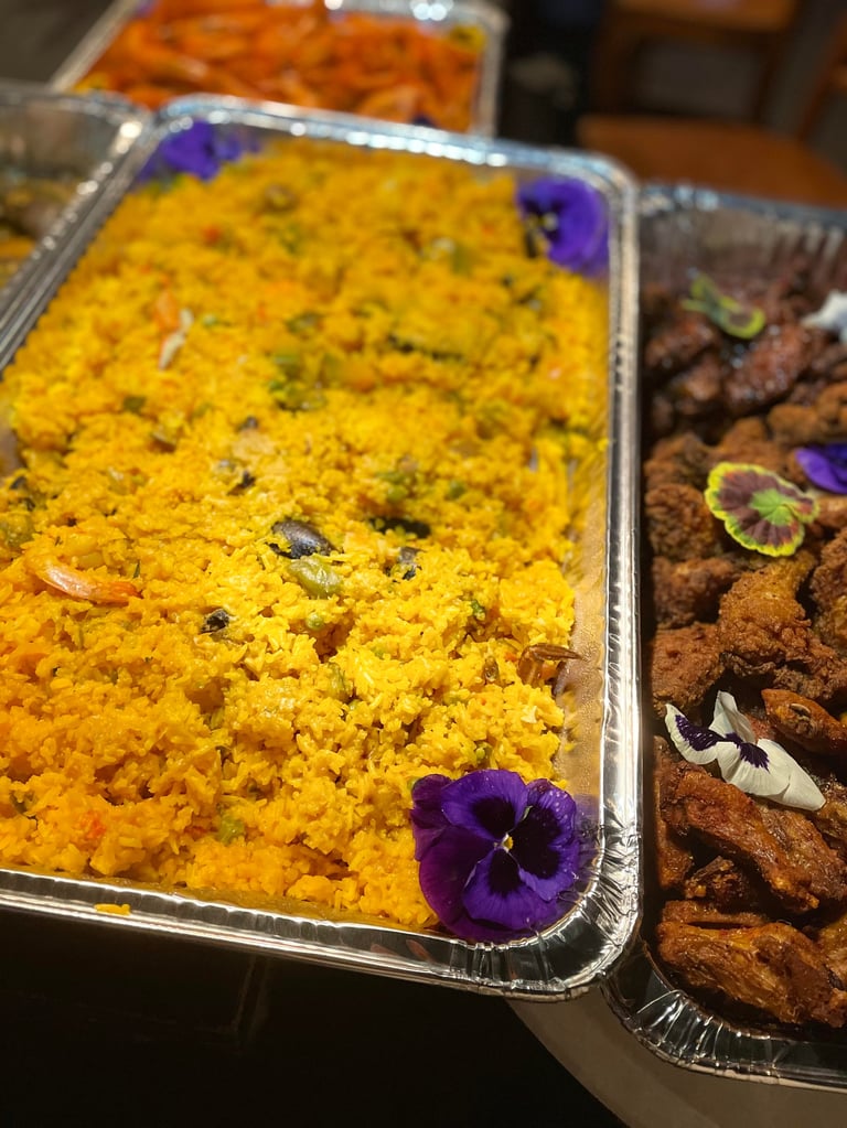 Catering trays with golden yellow rice dish garnished with purple flowers and brown spiced food items decorated with edible flowers