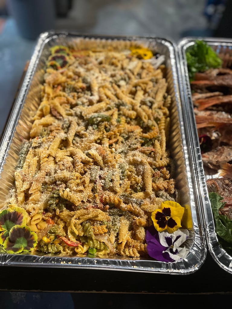 Aluminum tray of seasoned pasta salad with edible flowers garnish at a catered event