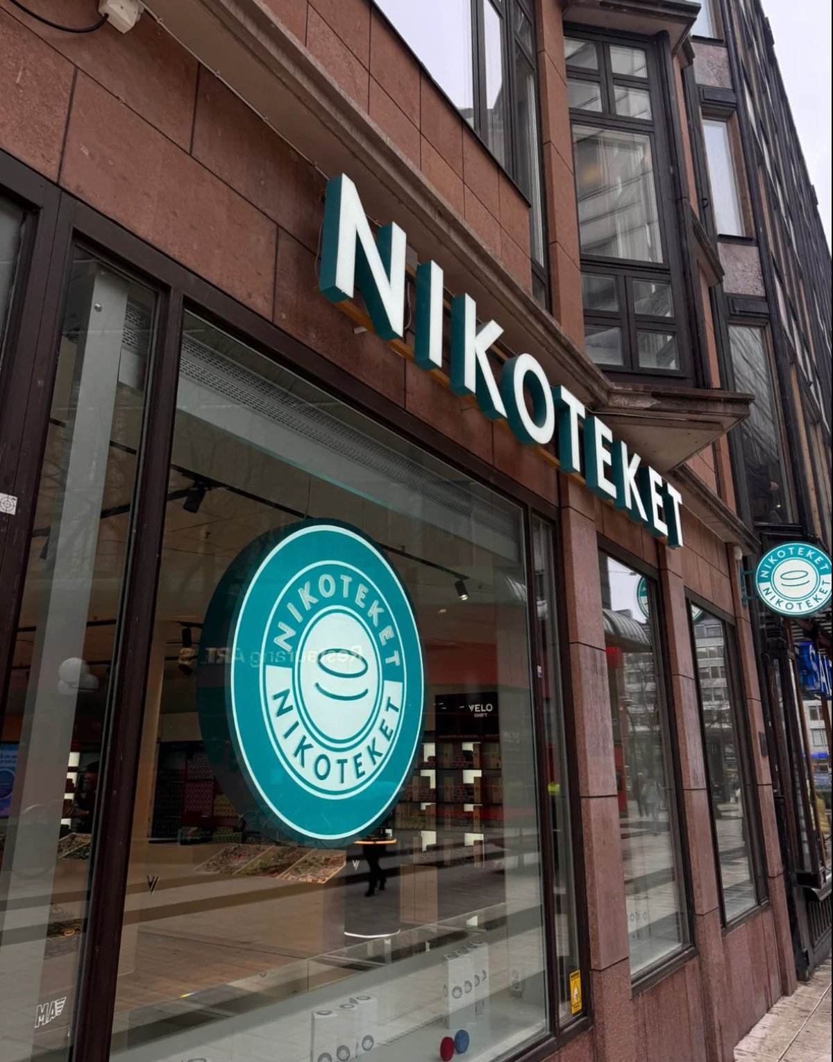 Storefront of Niko Teket restaurant with teal circular logo on window and white signage on red brick building facade