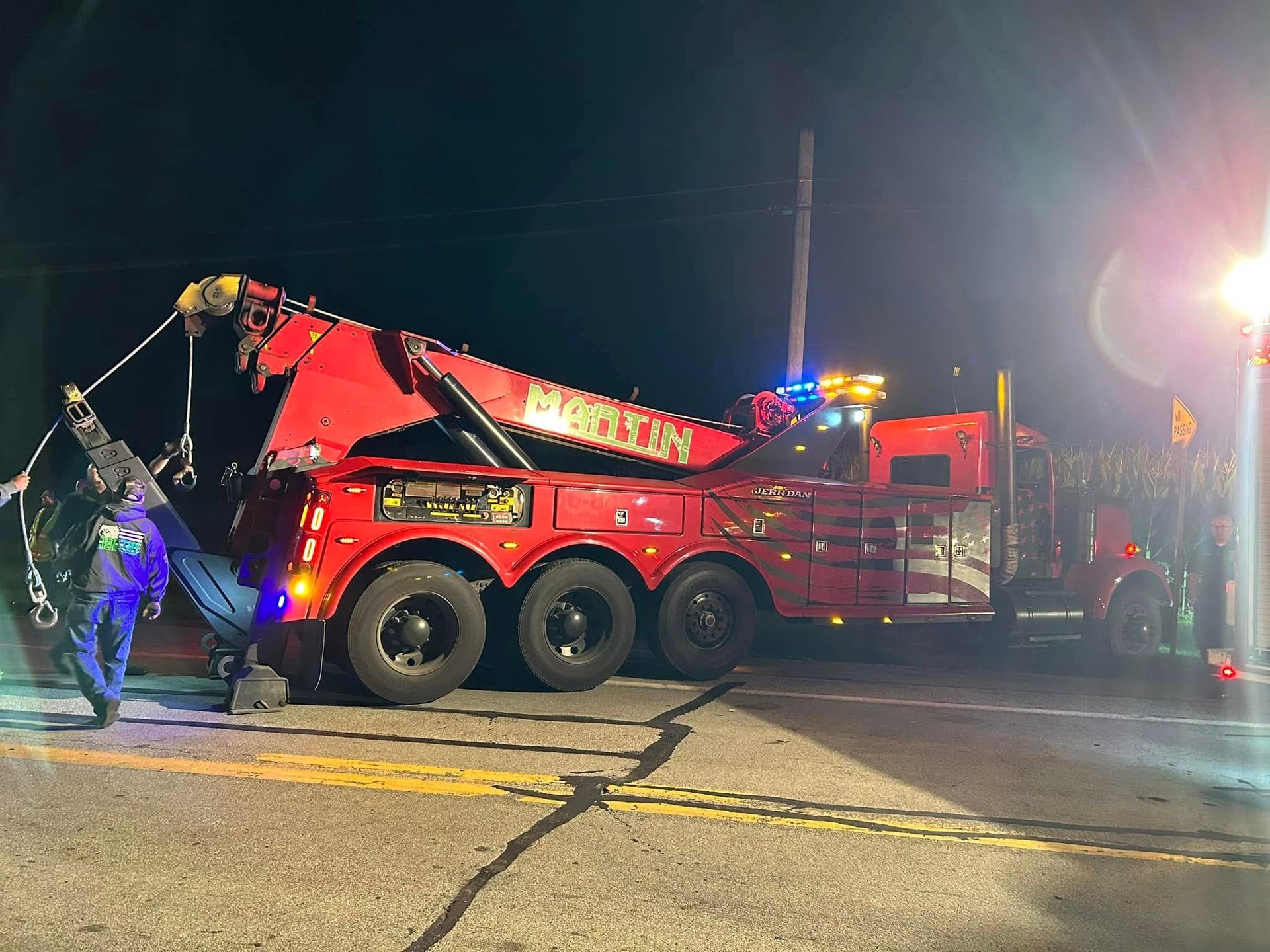 Red towing truck with hydraulic crane lifting a vehicle at night