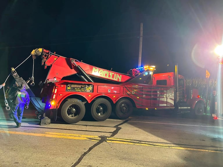 Red towing truck with hydraulic crane lifting a vehicle at night on a street