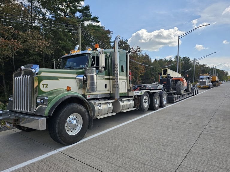 Large green and white semi-truck with number 12 on cab, leading a convoy of trucks on a paved road