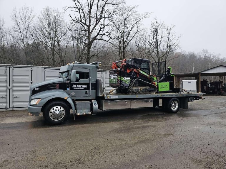 Flatbed tow truck with red and green equipment loaded, parked in industrial yard
