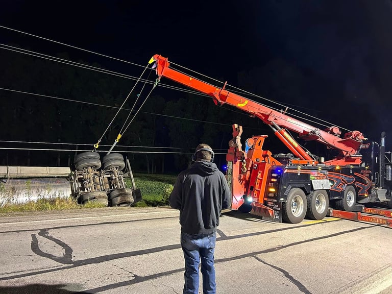 Red rotator wrecker with extended boom recovering an overturned vehicle at night