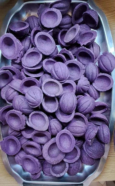 Purple round biscuits or cookies piled in a white oval baking tray on a wooden surface