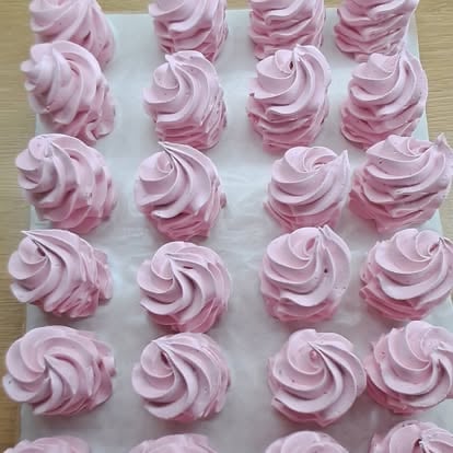 Pink and white swirled frosting piped onto white parchment paper in rows on a wooden surface