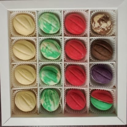 Assorted chocolate truffles in a 4x4 grid box with vanilla, green, red, and brown flavored candies in paper liners