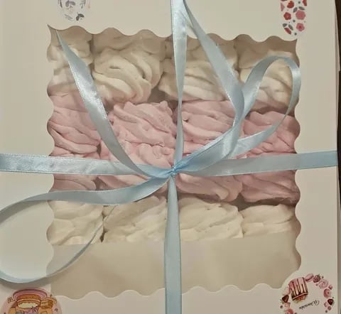 Gift box with pink and cream colored macarons tied with a blue ribbon bow