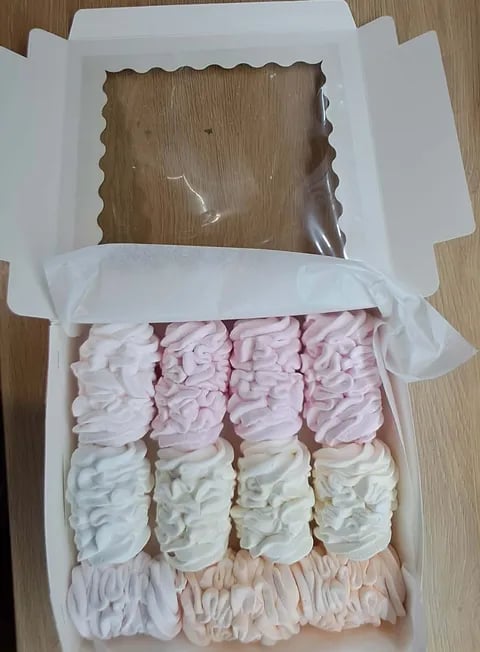 Open white box containing assorted pastel-colored meringue cookies arranged in rows on tissue paper