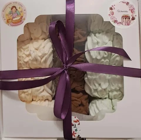 Gift-wrapped assorted cookies in a box tied with purple ribbon, displayed with decorative floral stickers on white background