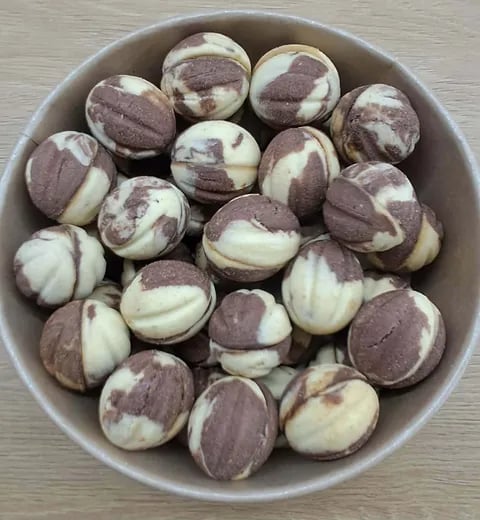 A white bowl filled with chocolate and vanilla swirl cookies arranged in a circular pattern on a wooden surface