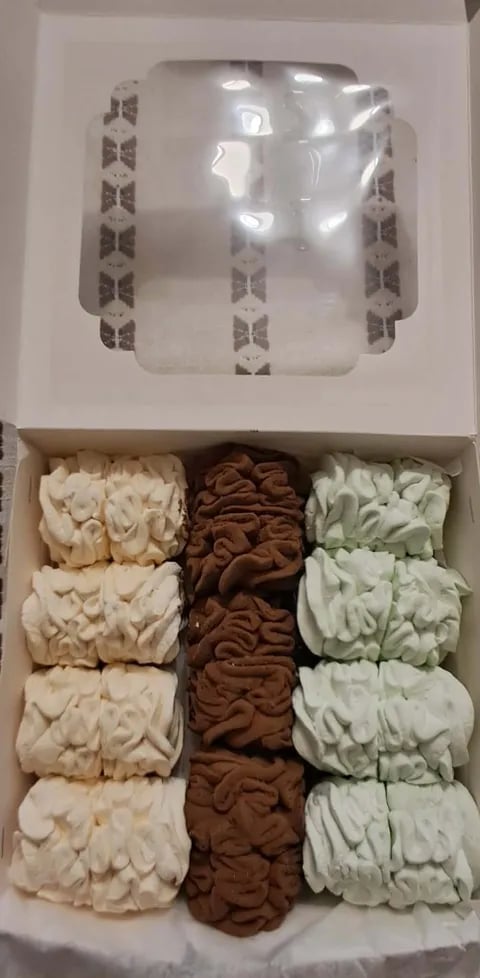 Box of assorted meringue cookies in vanilla, chocolate, and pistachio flavors arranged in three columns