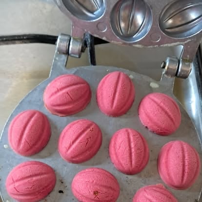 Pink round macarons with ridged tops on parchment paper in a baking tray with oven mitts above