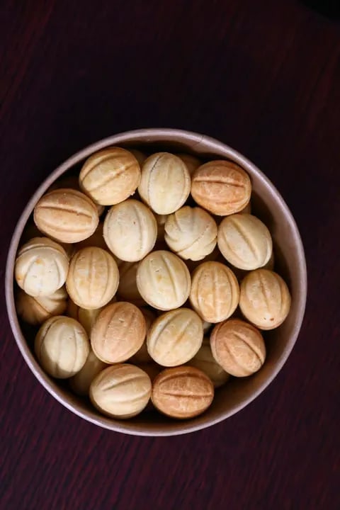 Overhead view of shelled walnuts in a metallic bowl on a dark wooden surface
