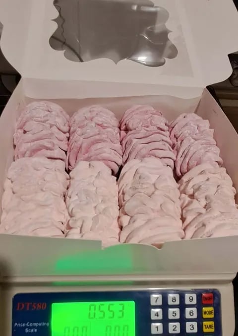 Box of pink and white meringue cookies arranged in rows on a digital scale displaying 85.57