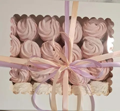Square gift box filled with pink piped meringue cookies tied with pale pink and purple ribbon bows