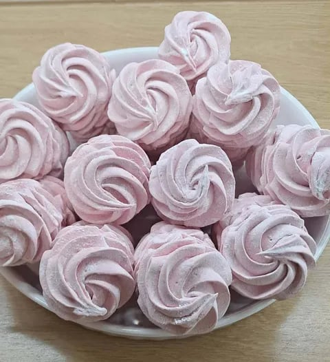 Pink and white swirled meringue cookies arranged on a white plate