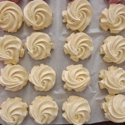 Sixteen vanilla piped rosette cookies arranged in rows on parchment paper