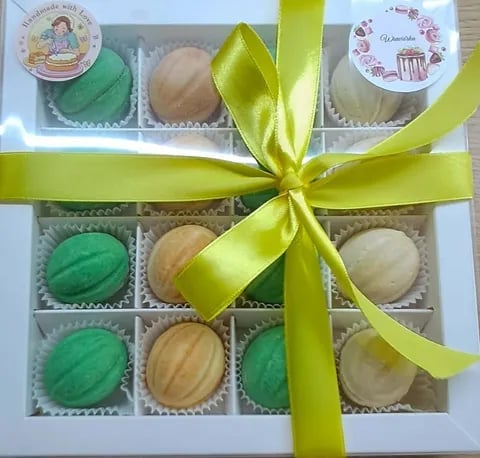 Box of assorted macarons tied with a bright yellow-green ribbon bow, featuring green and beige colored cookies in paper liners