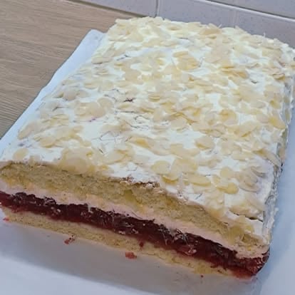 Layered sheet cake with sliced almonds on top, jam filling, and vanilla sponge cake on white plate