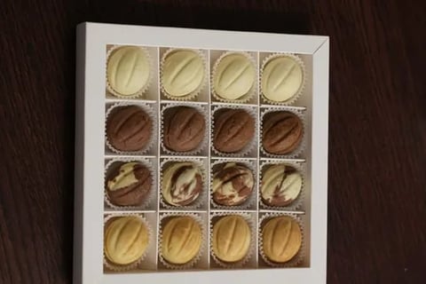 Box of 16 assorted chocolates arranged in rows, featuring white, dark, and milk chocolate varieties with various toppings and drizzles