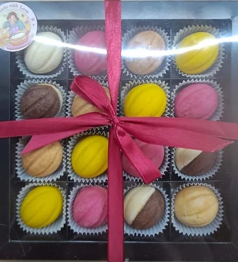 Gift box of 16 assorted bonbons with colored frosting in pink, white, yellow, and brown, tied with a pink ribbon bow