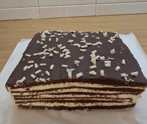 Rectangular chocolate layer cake with sliced almonds on top, displayed on white paper in a tiled kitchen