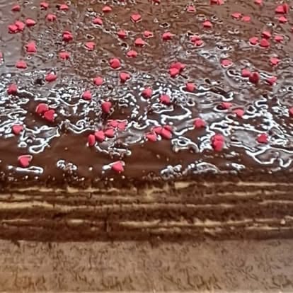Close-up of a chocolate dessert topped with white drizzle and pink candies or sprinkles on a textured surface