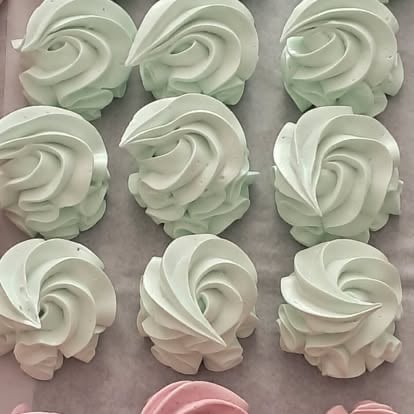 Nine pale green and white piped meringue or buttercream rosettes arranged in three rows on parchment paper