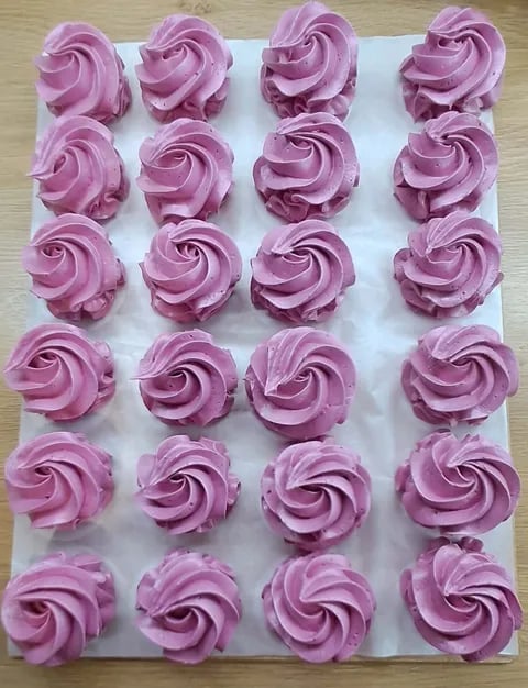 Twenty-four pink frosted cupcakes arranged in rows on white parchment paper