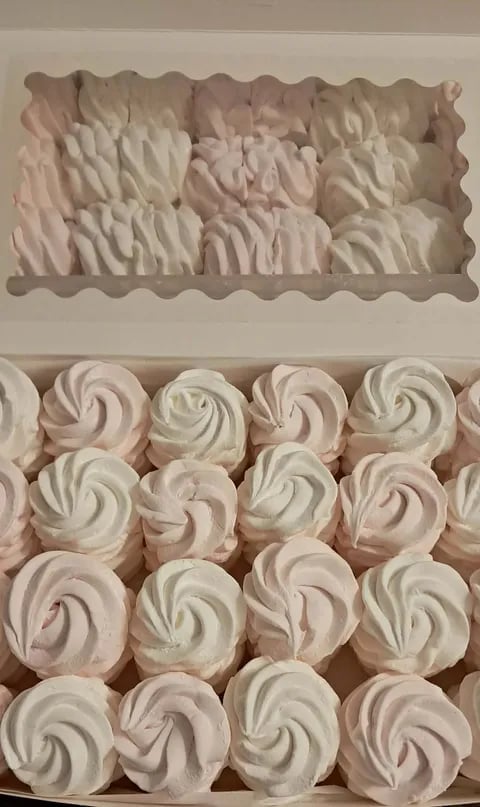 Assorted swirled meringue cookies and swirled frosting piping in white and pale pink displayed on white background