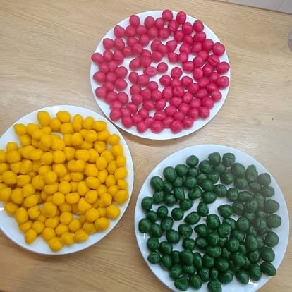 Three white plates filled with red, yellow, and green round candies or balls arranged on a wooden surface