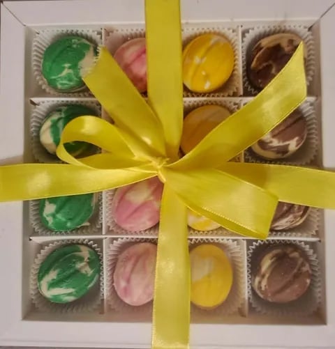 Box of assorted chocolates with yellow ribbon bow, featuring green, pink, yellow, and brown decorated truffles