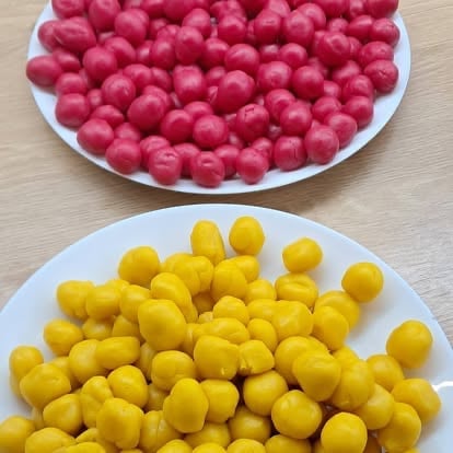 Two white plates filled with round pink and yellow candies on a beige wooden surface