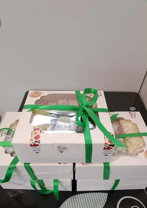 Stack of white bakery boxes tied with green ribbons on a black surface