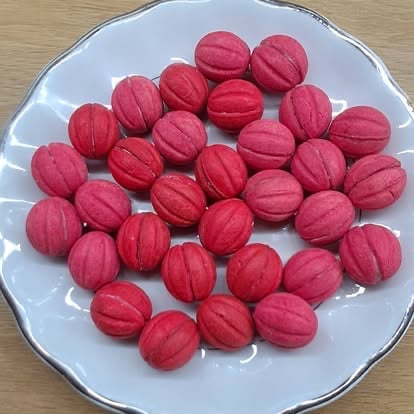 Red macaron cookies arranged on a white plate with decorative rim on a wooden surface