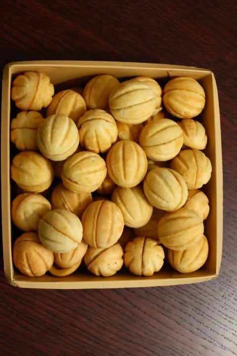 Box of golden shell-shaped butter cookies with ridged pattern on dark wooden surface