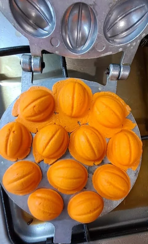 Orange-shaped waffle maker with twelve cooked orange-colored waffles arranged on the blue cooking plate