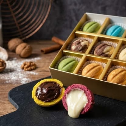 Colorful macarons displayed on a black slate with a box of assorted flavored macarons in the background on a wooden surface