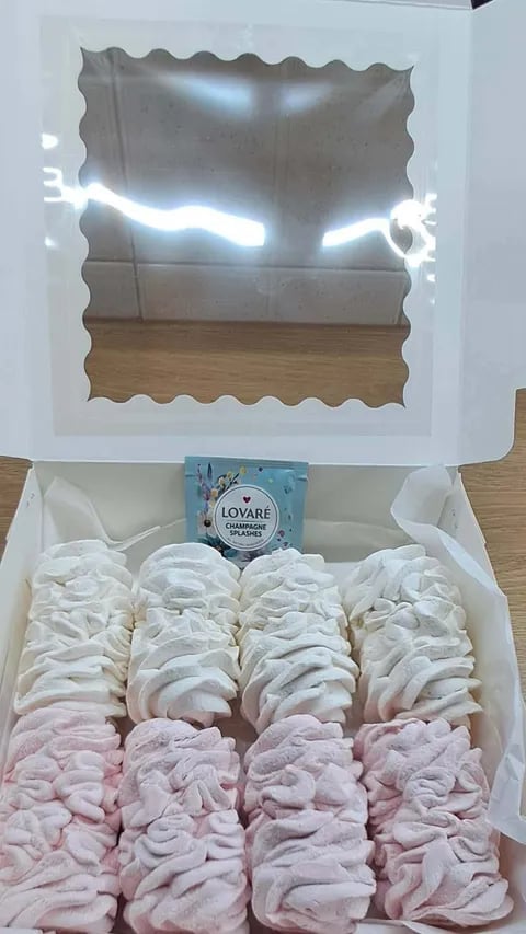 Open gift box with decorative window showing flowers, containing white and pink fabric scrunchies arranged in rows with a blue Lovare tea packet