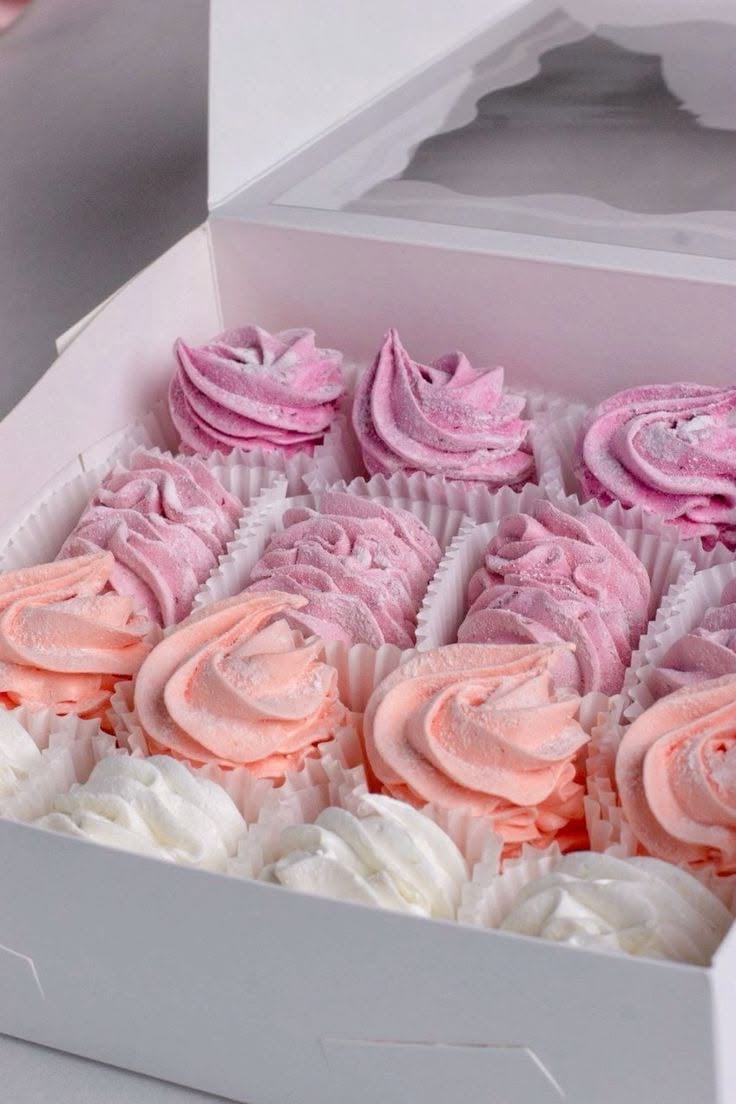 White box of frosted cupcakes in pink, salmon, and white with piped rosette frosting designs