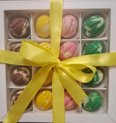 Assorted handmade chocolates in a gift box with yellow ribbon bow, featuring brown, pink, yellow, and green marbled truffles