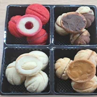Four compartments of assorted sandwich cookies: pink jam-filled cookies, chocolate cake rounds, white cream-filled cookies, and peanut butter cookies