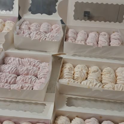 Assorted pastel-colored meringue cookies and macarons arranged in open white pastry boxes