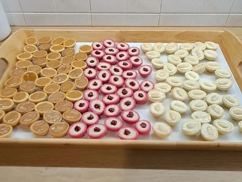 Wooden tray with assorted glazed donuts arranged in three columns: caramel-colored on left, pink frosted with jam centers in middle, and white frosted on right