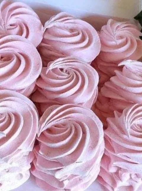 Close-up of pink and white swirled meringue cookies or whipped cream rosettes on a white surface