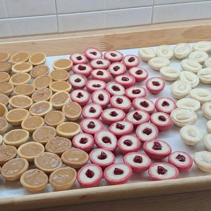 Assorted donuts arranged in rows: glazed, jam-filled pink, and coconut-covered varieties on a white tray
