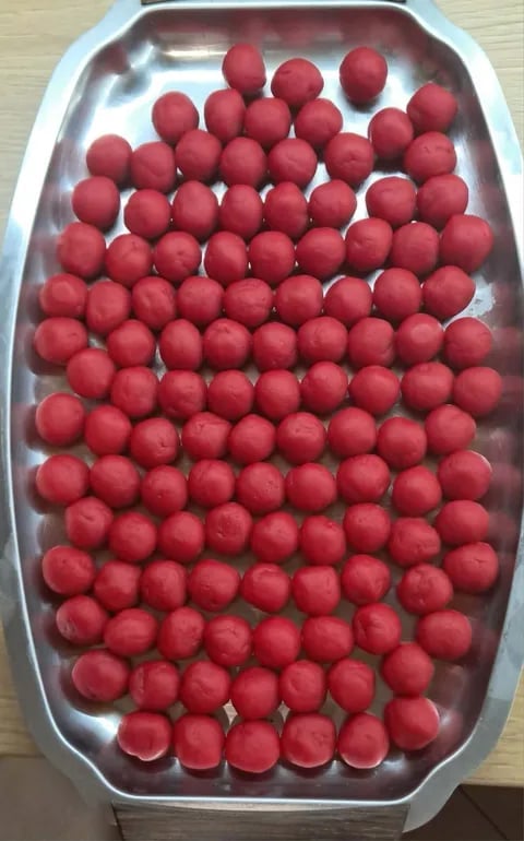 Over 100 red round candies or truffles arranged in rows on a white cardboard tray