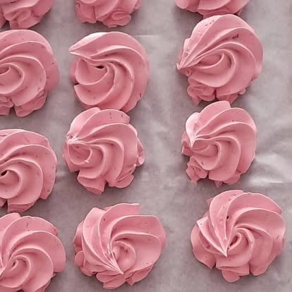 Pink piped meringue kisses arranged on parchment paper, showing swirled frosting texture in rows