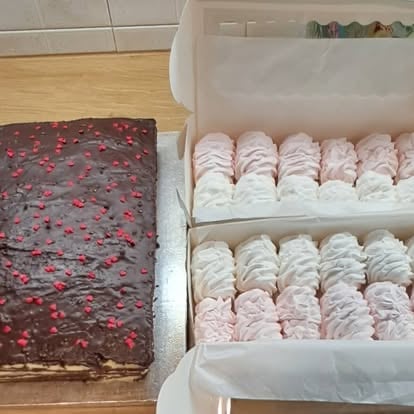 Chocolate berry cake next to a box of pink and white frosted cupcakes on a kitchen counter
